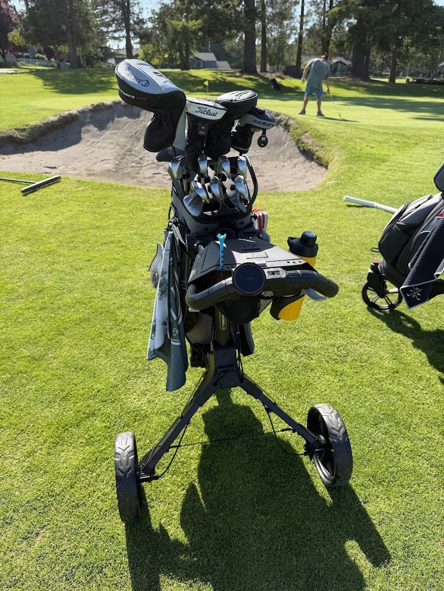 Alphard Cybercart Push+ golf push cart in black and yellow on course fairway fully loaded with golf bag clubs and accessories